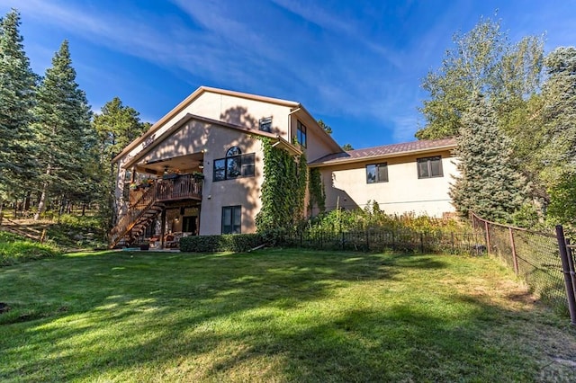 rear view of property with stairway, fence, stucco siding, a deck, and a lawn