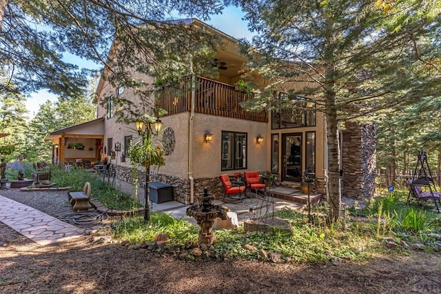 back of house featuring stucco siding, stone siding, and a patio area