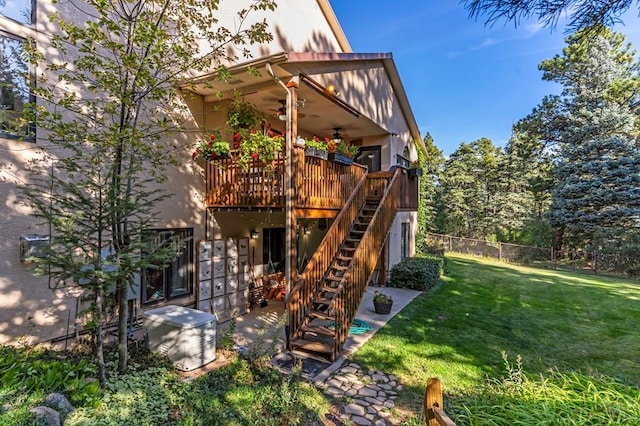 rear view of house featuring fence, stairway, a wooden deck, a lawn, and a ceiling fan