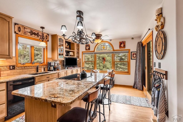 kitchen featuring light wood-type flooring, a kitchen island, a sink, black appliances, and tasteful backsplash