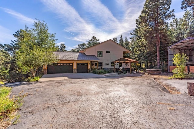 view of front of property featuring a gazebo, an attached garage, stone siding, and driveway