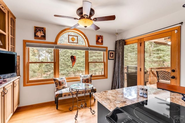 kitchen featuring light wood-style flooring, a ceiling fan, light stone counters, baseboards, and stove