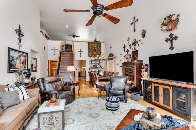 living area with a high ceiling, stairs, ceiling fan, and wood finished floors