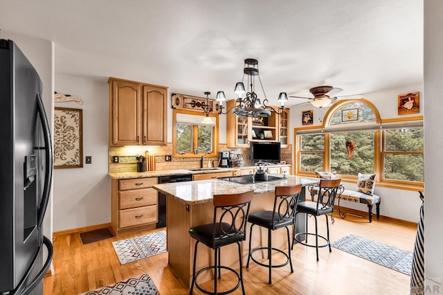 kitchen with a kitchen island, refrigerator with ice dispenser, dishwashing machine, black electric cooktop, and a sink