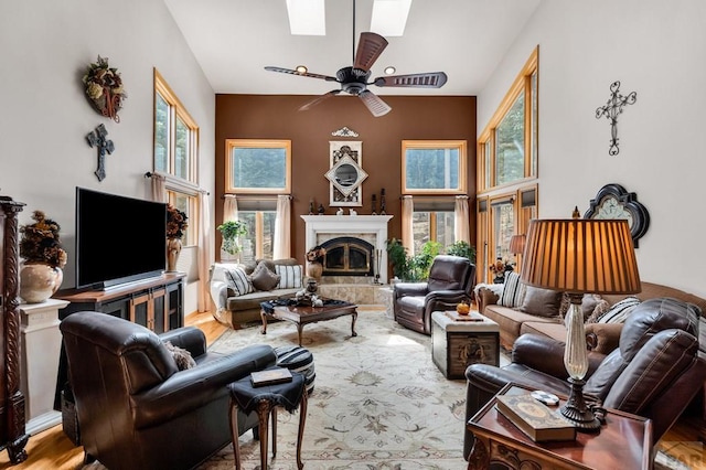 living area with ceiling fan, plenty of natural light, a skylight, and a fireplace