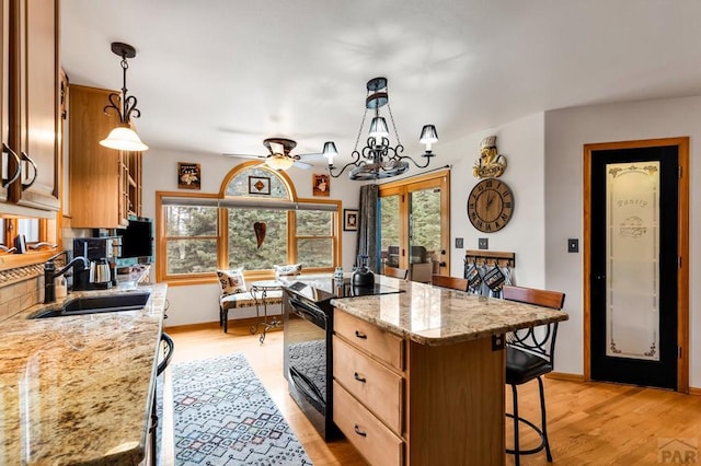 kitchen with light wood-type flooring, a breakfast bar, black electric range oven, a sink, and a center island