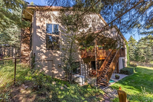 back of property featuring stucco siding, fence, a yard, and stairway