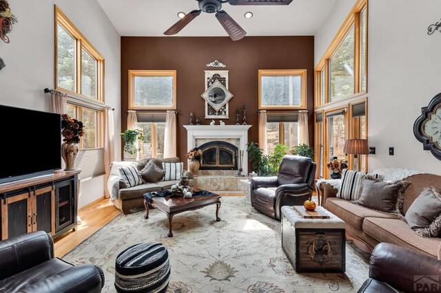 living room with a tiled fireplace, a towering ceiling, a ceiling fan, and wood finished floors