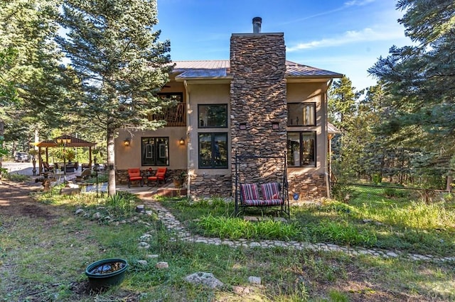 back of property with a balcony, a chimney, stucco siding, stone siding, and a patio area