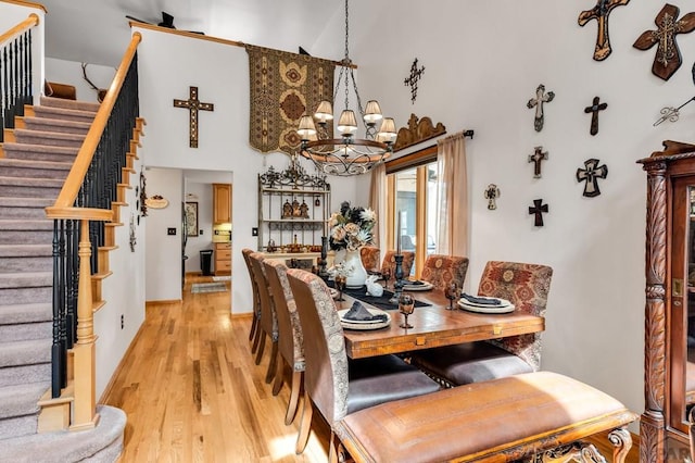 dining space with light wood-type flooring, a notable chandelier, a high ceiling, baseboards, and stairs