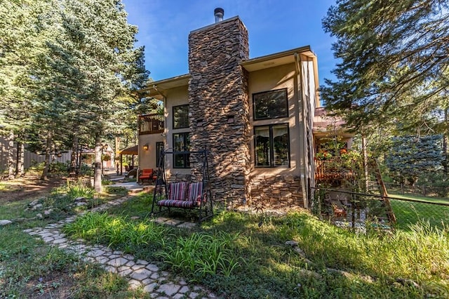 back of property with a balcony, fence, stone siding, and stucco siding