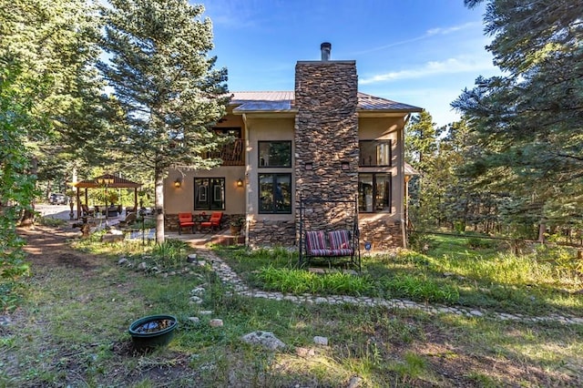 rear view of house with a patio, a balcony, a chimney, stucco siding, and stone siding