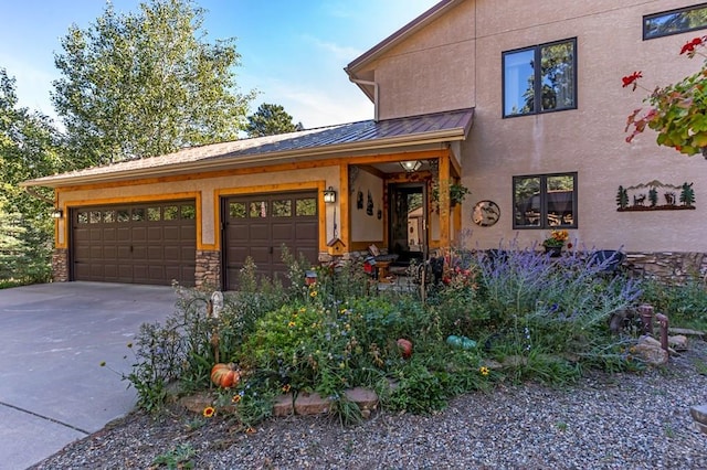 view of front of house featuring concrete driveway, metal roof, a garage, stone siding, and a standing seam roof