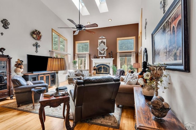 living area with high vaulted ceiling, a glass covered fireplace, a skylight, and wood finished floors