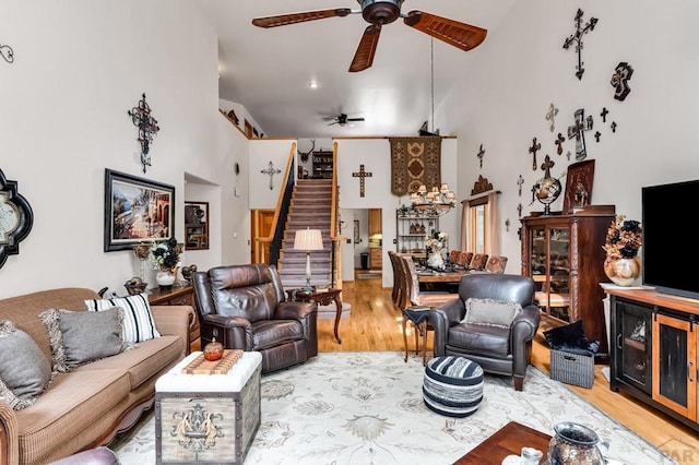 living room featuring stairway, wood finished floors, a ceiling fan, and a towering ceiling