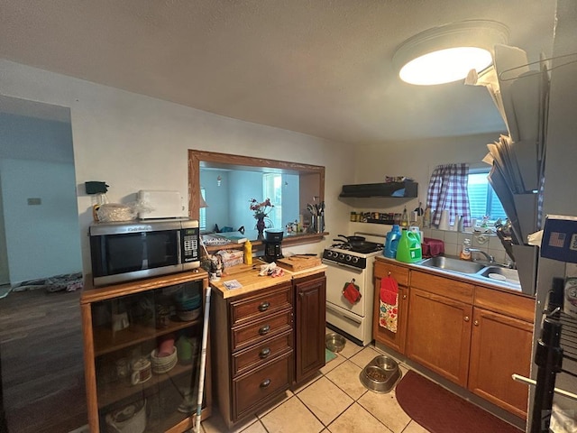 kitchen featuring stainless steel microwave, light tile patterned floors, white gas range, under cabinet range hood, and a sink