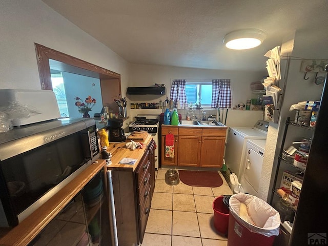 kitchen with stainless steel microwave, separate washer and dryer, white gas range oven, light countertops, and a sink
