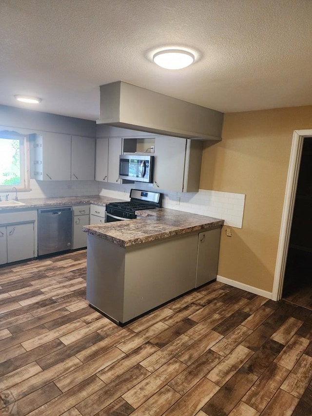 615 San Juan St, Trinidad, CO 81082 - kitchen featuring stainless steel appliances, a peninsula, a textured ceiling, and dark wood-type flooring