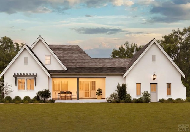 back of property at dusk with a lawn and stucco siding