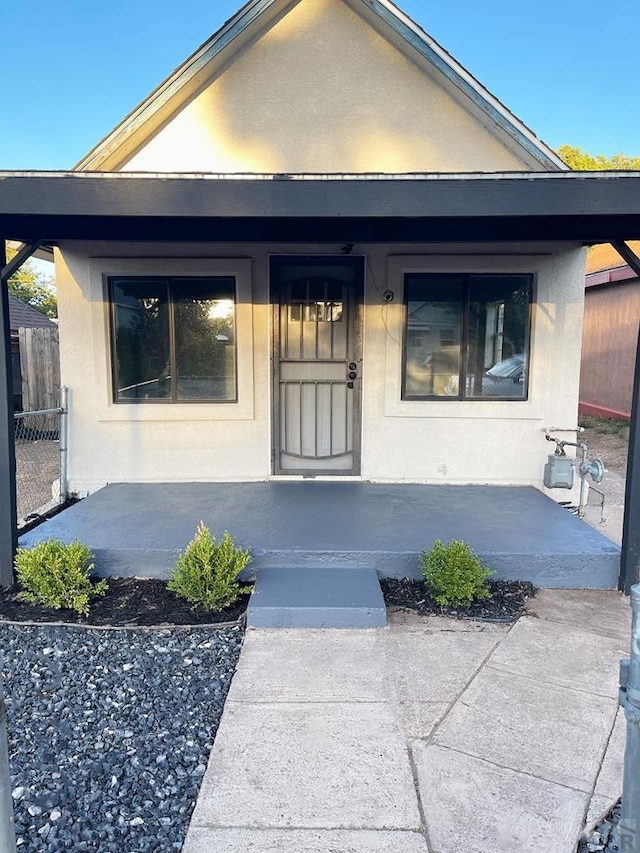 doorway to property with fence, a porch, and stucco siding