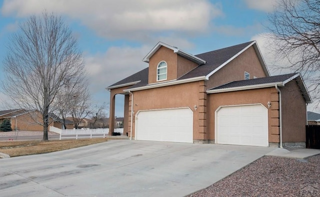 view of front facade with stucco siding, driveway, a garage, and fence