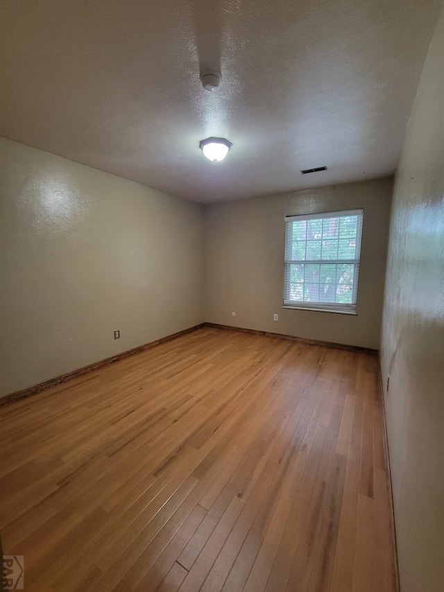 spare room featuring light wood-type flooring, visible vents, a textured ceiling, and baseboards