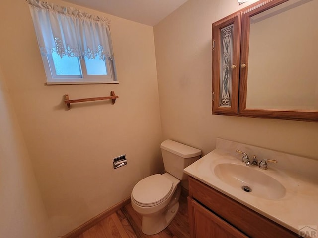 half bathroom featuring baseboards, vanity, toilet, and wood finished floors