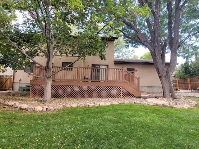 rear view of property with a deck, a yard, fence, and stucco siding