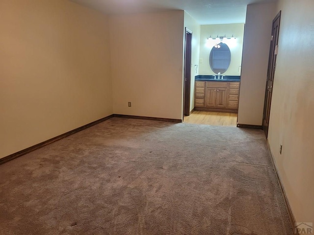 unfurnished room featuring light carpet, baseboards, and a sink