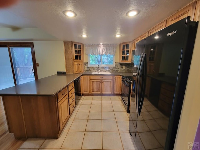 kitchen with a peninsula, a sink, black appliances, dark countertops, and glass insert cabinets