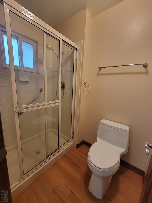 bathroom featuring baseboards, wood finished floors, toilet, and a shower stall