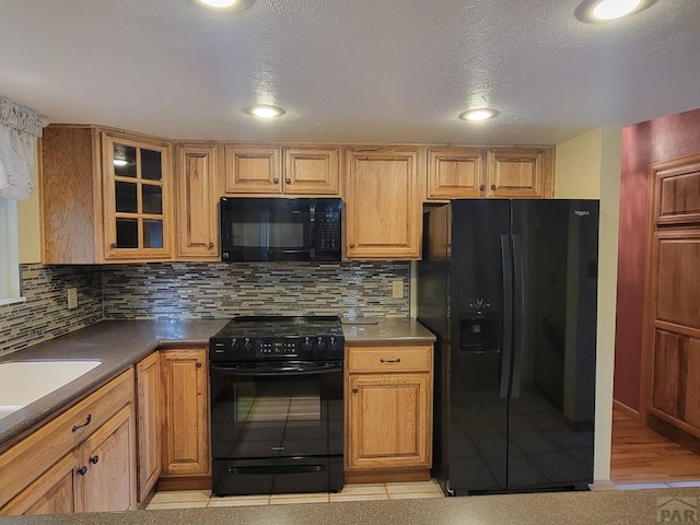 kitchen featuring black appliances, tasteful backsplash, light tile patterned floors, and glass insert cabinets