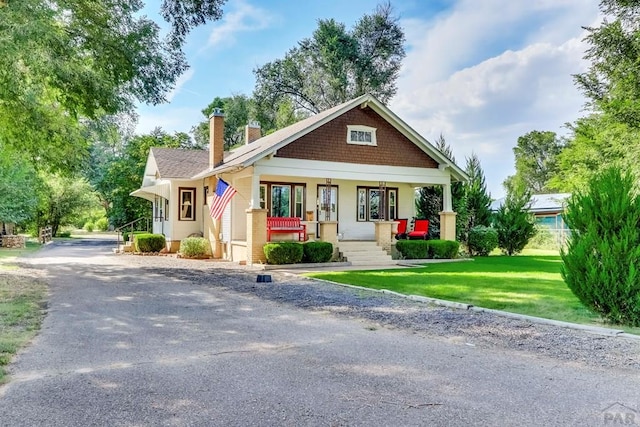 view of front of home with a porch, a front yard, and a chimney