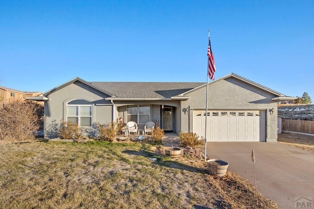 ranch-style home featuring an attached garage, fence, concrete driveway, stucco siding, and a front yard