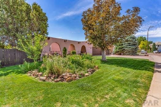 pueblo-style house with a garage, fence, driveway, and a front lawn