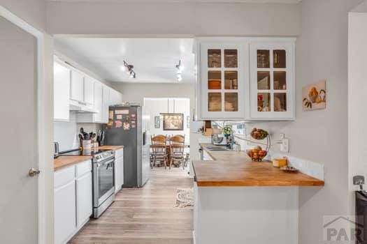 kitchen with under cabinet range hood, stainless steel appliances, butcher block countertops, white cabinetry, and glass insert cabinets