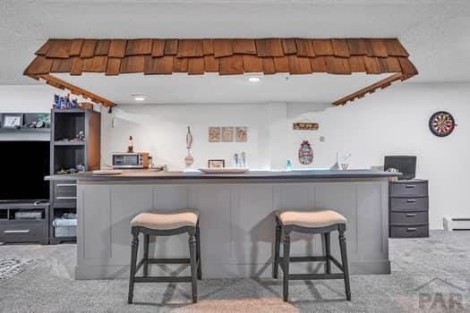 bar with wet bar, stainless steel microwave, light carpet, and a baseboard radiator