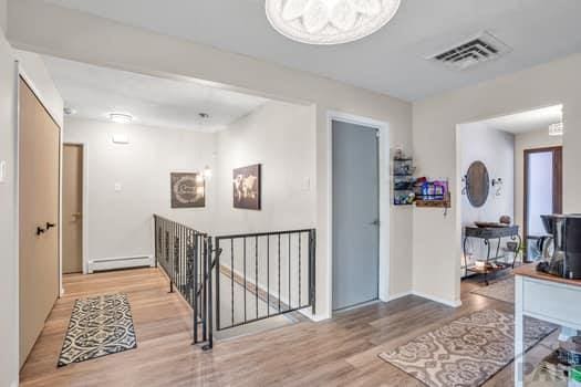 hall featuring visible vents, baseboard heating, wood finished floors, and an upstairs landing