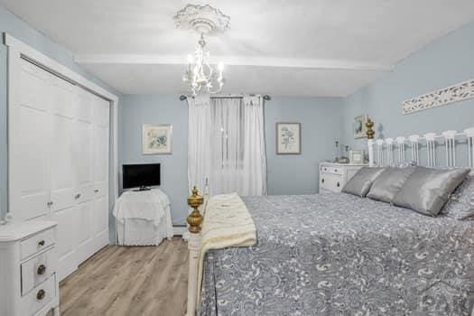 bedroom featuring a closet, baseboard heating, a chandelier, light wood-type flooring, and beamed ceiling