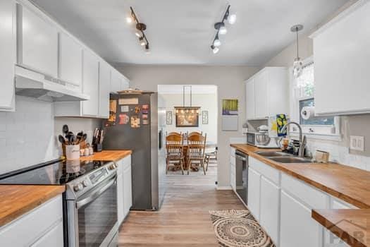 kitchen with decorative light fixtures, stainless steel appliances, white cabinets, a sink, and under cabinet range hood