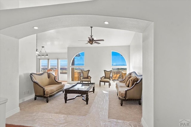 living area featuring baseboards, arched walkways, a ceiling fan, and light colored carpet