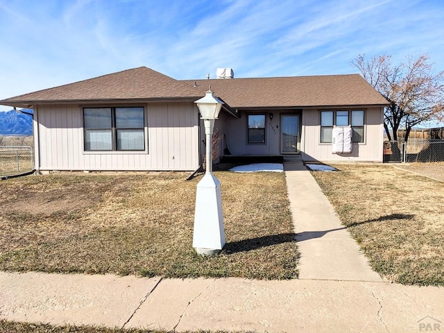 view of front of property with a shingled roof, fence, and a front lawn