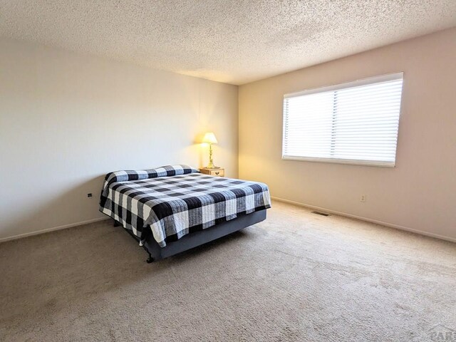 bedroom featuring carpet flooring, visible vents, a textured ceiling, and baseboards