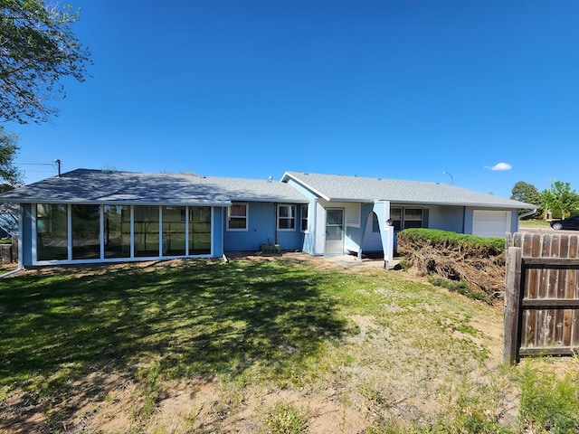 back of property with a yard, a shingled roof, an attached garage, and fence