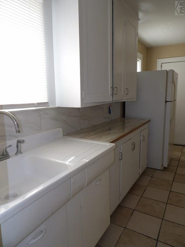 kitchen with light tile patterned floors, light countertops, backsplash, freestanding refrigerator, and white cabinets