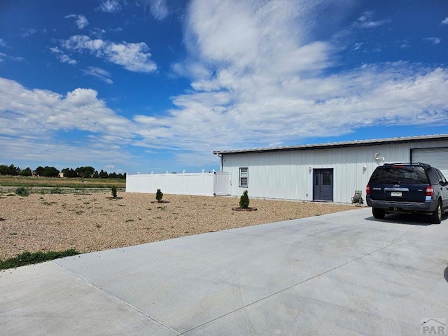 view of outdoor structure with a garage, concrete driveway, an outdoor structure, and fence