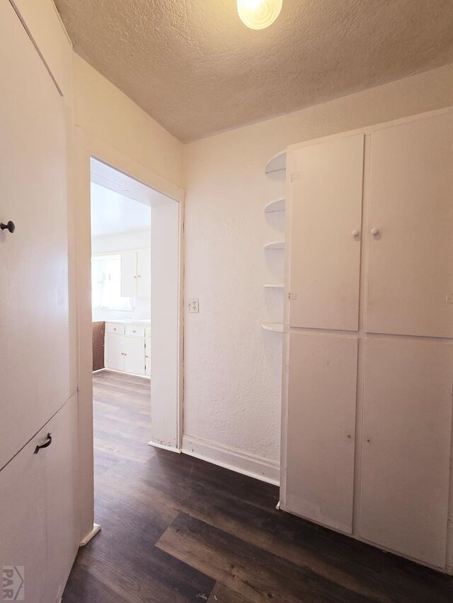 hall featuring a textured ceiling, dark wood-type flooring, and baseboards