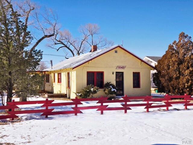 snow covered property with a fenced front yard, a chimney, and stucco siding