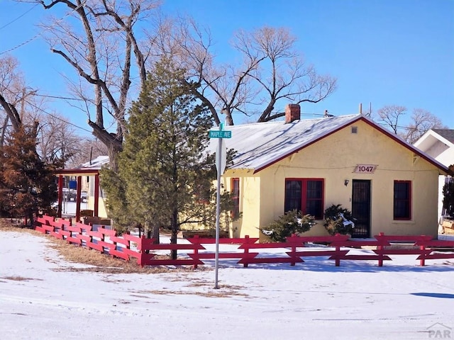 snow covered rear of property with a fenced front yard, a chimney, and stucco siding