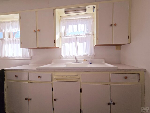 kitchen with white cabinetry, light countertops, and a sink